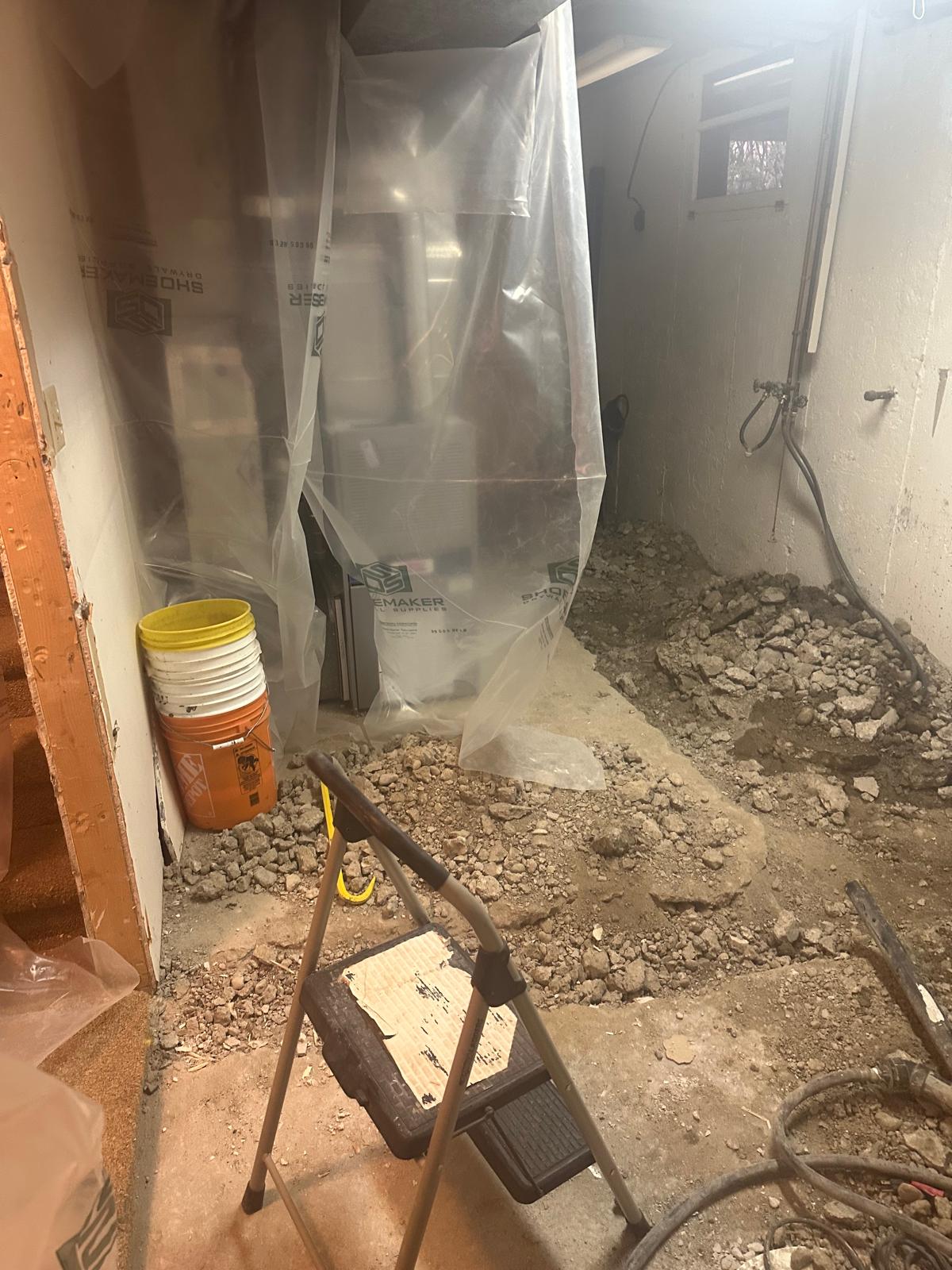 Basement mechanical room with concrete floor broken out for plumbing rough-in and parging repair on the foundation wall, furnace masked off in plastic