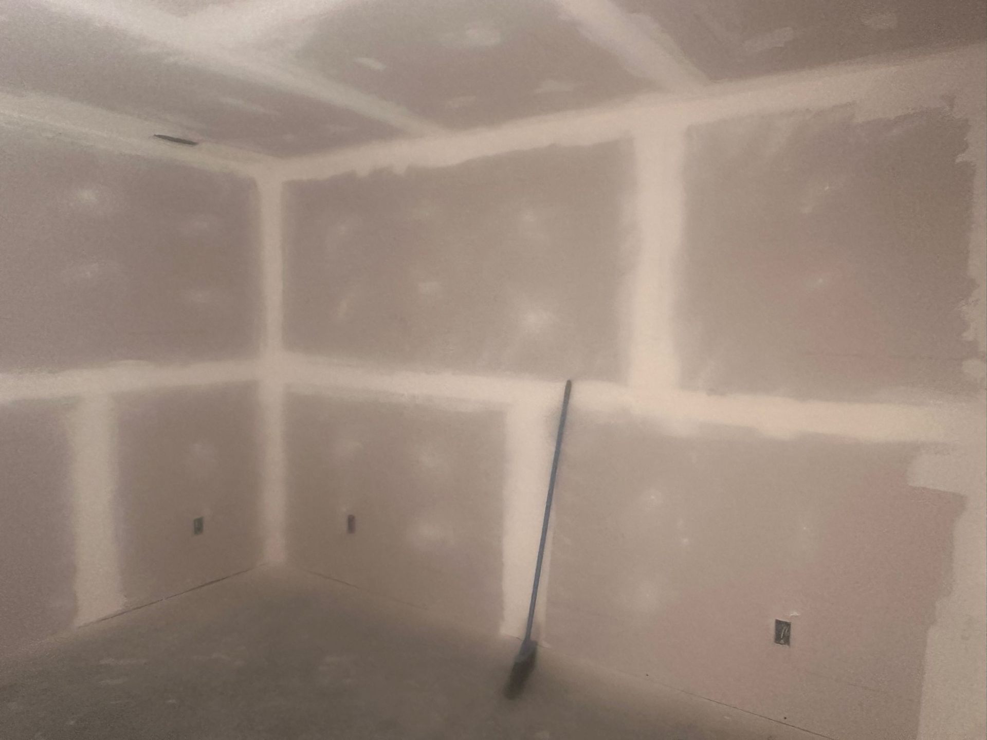 Basement room fully boarded with drywall, seams taped and mudded, ready for sanding and primer