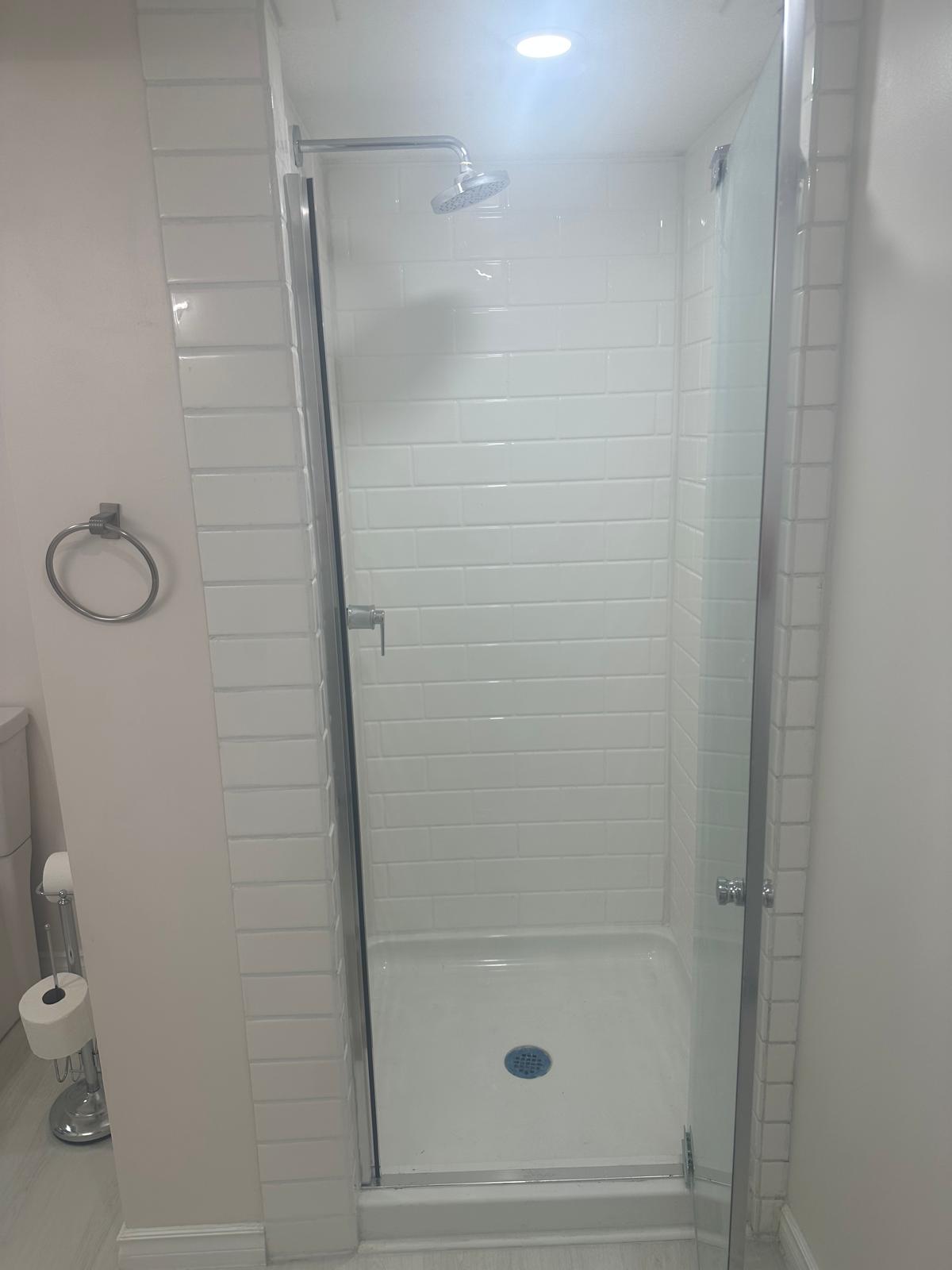 Inside the basement shower enclosure — full-height subway tile, chrome rain showerhead and pressure-balance valve