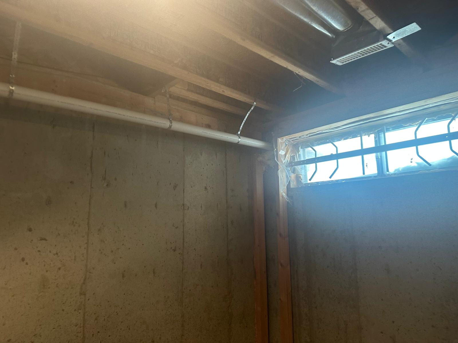 Original unfinished basement with bare concrete foundation walls and small builder window before egress upgrade
