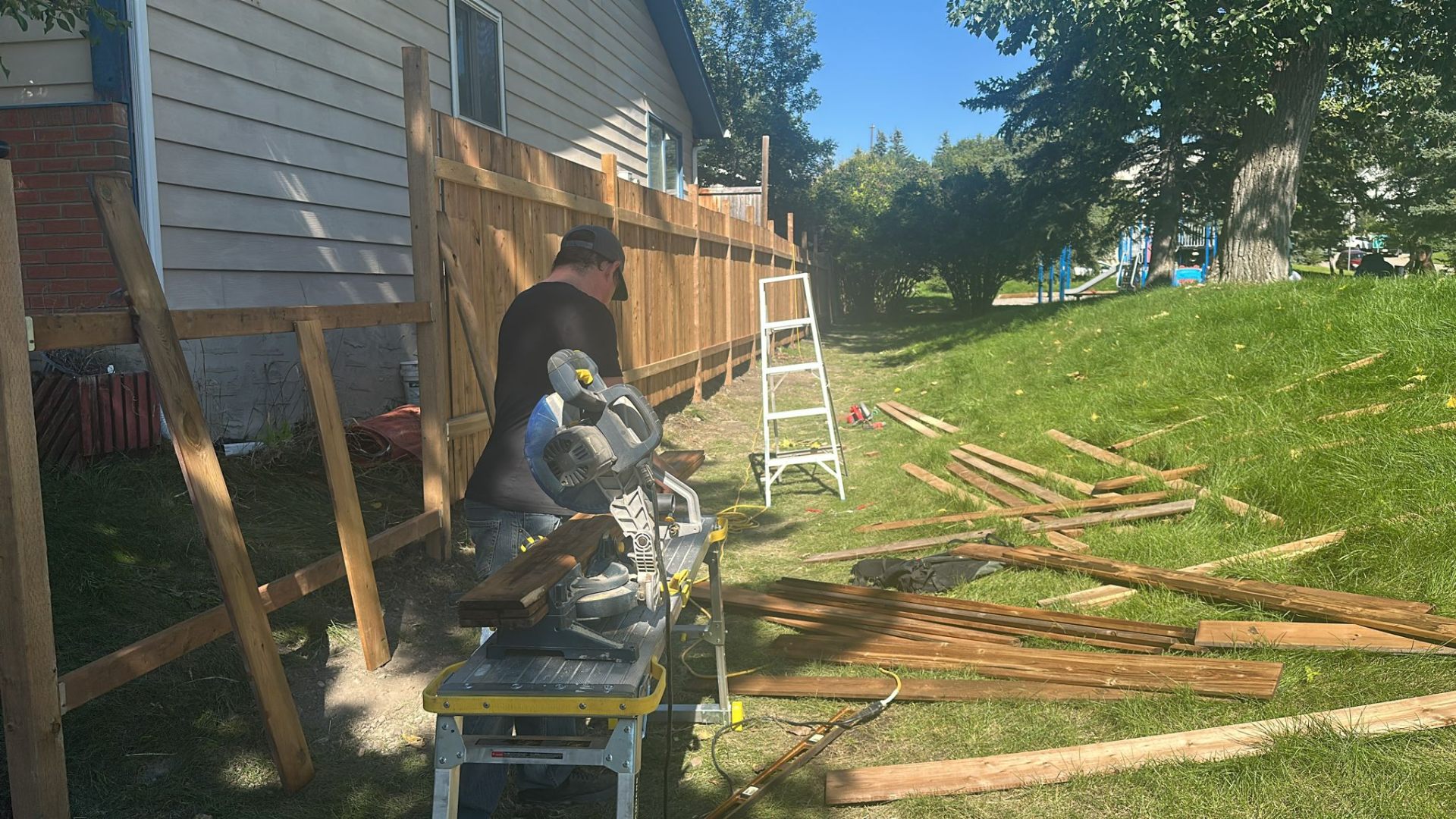 OmniPro craftsman cutting cedar fence boards on a mitre saw during a privacy fence build in Calgary