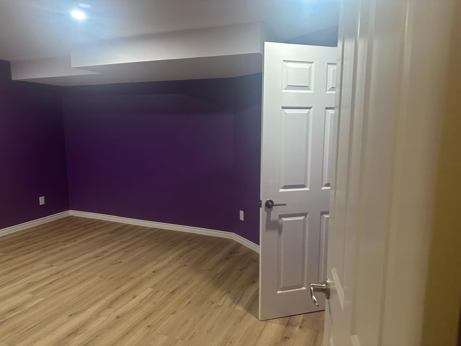 Deep purple accent wall against white ceiling and trim in a finished basement room
