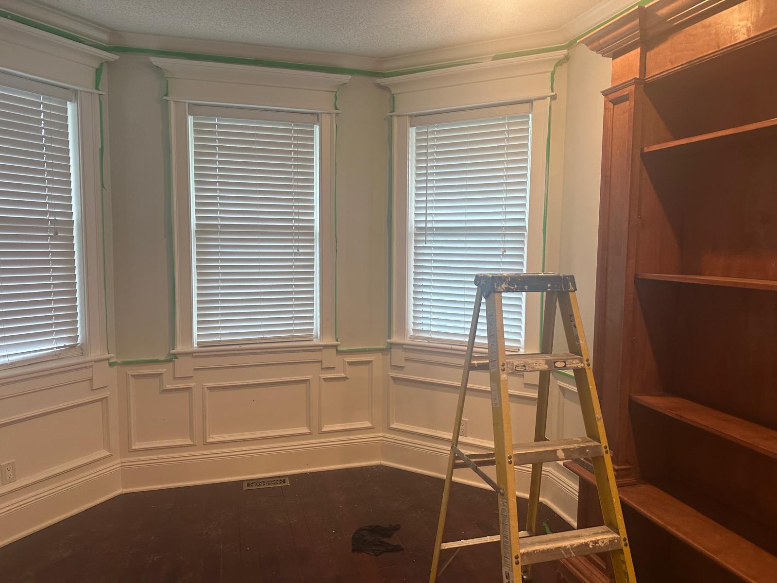 Heritage bay window with detailed white wainscoting and trim, freshly masked and painted